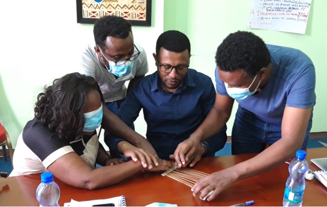 A group of participants engaging in a group exercise titled You think - I feel involving a visually impaired person in a group activity by directing their hands.